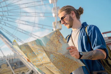 Handsome young man in casual clothing looking at map while walking outdoors. Hipster looking for a...