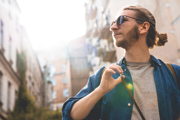 Close up shot of handsome young man in casual clothing looking at view while walking through city streets. Modern caucasian tourist adventurer on a solo trip - obrazy, fototapety, plakaty