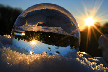 Winter sunset with snow as seen in a lens ball with starburst sun. Concept for environment background