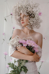 Portrait of sensual blond woman with flowers. Beautiful girl with flowers in her hair. Summer Beauty. Art in a contemporary style. A gypsophila wreath on a white background. Perfume, cosmetics concept