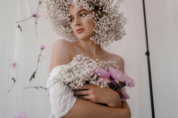 Portrait of sensual blond woman with flowers. Beautiful girl with flowers in her hair. Summer Beauty. Art in a contemporary style. A gypsophila wreath on a white background. Perfume, cosmetics concept