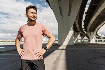 Fototapeta premium Confident man pausing after a run under an urban bridge, reflecting determination.