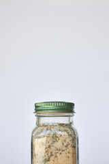 Jar of garlic, salt and herbs seasoning. close-up Glass container with closed green aluminum lid on gray background, recyclable packaging. Copy space. Cooking courses concept, order in kitchen, spices