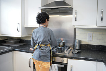 Little kid is learning how to cook at home wearing aprons in the morning time. - obrazy, fototapety, plakaty