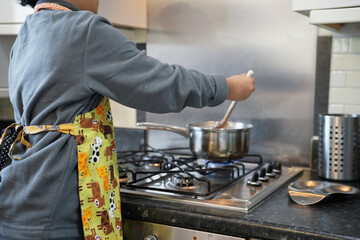 Little kid is learning how to cook at home wearing aprons in the morning time. - obrazy, fototapety, plakaty