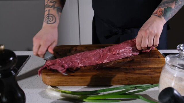 the chef cuts the meat on a wooden chopping board, preparing it for further cooking. The cook cuts out the excess parts to a piece of juicy pork meat