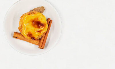 One Portuguese Pastel de Nata pie with custard and cinnamon sticks on a white plate. Pastel de Belem is an iconic cup-shaped pastry with a burnt top and a crispy puff pastry crust. Sweet dessert.