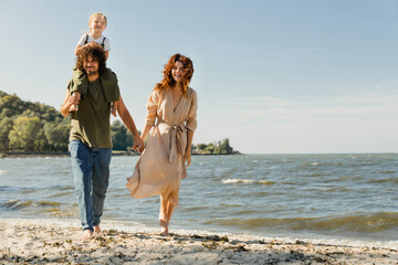 Caucasian family of mother and father carrying daughter on his shoulders on vacation on the beach