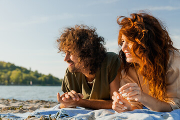 Happy smiling caucasian couple relaxing on the beach, lying on blanket with look away