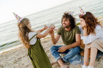 Happy family celebrating fathers birthday on a beach. Cute girl giving present box to her father.