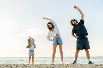Full length portrait of happy family doing morning workout on beach