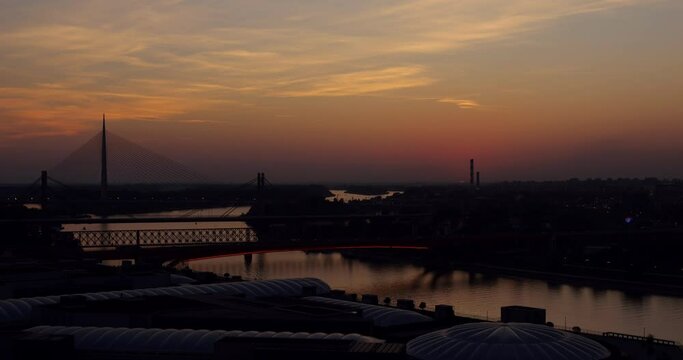 Time-lapse of serene autumn sunset in Belgrade. Bright yellow sun quickly descends and hide behind horizon, casting soft light over Ada Bridge and fast traffic of boats on Sava River