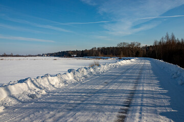 Cleaned winter road in the forest. Winter landscape with snow and blue sky. Road along the field and forest covered with snow and ice.