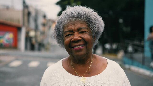 One happy black senior woman walking forward to camera in urban setting street. Gray hair elderly South American lady in 80s depicting active mature old age, portrait close-up