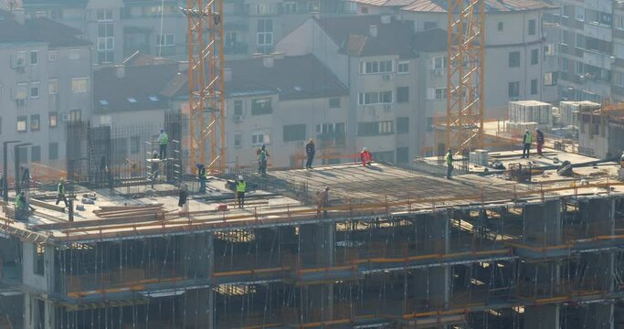 Construction workers labor on multi-story concrete building, telephoto view, time-lapse shot. High-level activities include formwork, reinforcement, and internal systems before concrete pouring.