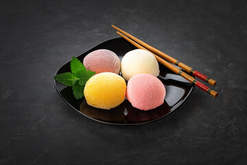 Mochi dessert on a black background in a black plate with mint leaves. There are bamboo sticks nearby. View from above. Perfect retouching.