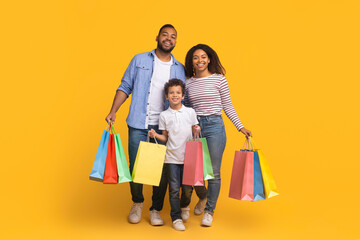 Delighted black family enjoying making shopping together, holding colorful paper bags