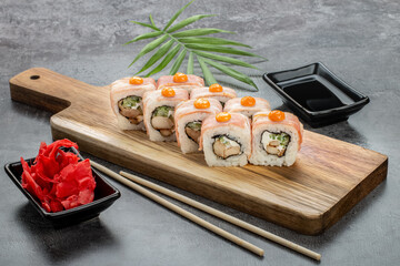 Rolls with bacon, chicken, cucumber and cream cheese on a wooden board. Ginger, soy sauce and bamboo sticks on a gray background. Top and side view.