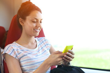 Pretty woman traveling by train sitting near the window using smartphone