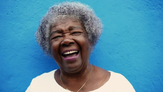 One happy senior African American elderly woman with gray hair laughing and smiling in blue wall backdrop. Portrait a joyful latin older person