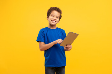 Smiling boy using digital tablet in blue shirt, yellow background - obrazy, fototapety, plakaty