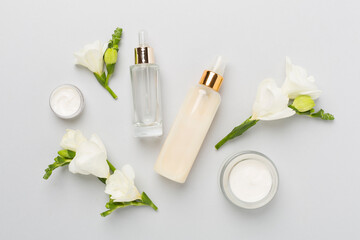 Facial cosmetic products with freesia flowers on color background, top view