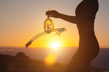 hand holds snorkeling goggles against the background of the sunset sky. Silhouette of a sexy woman...