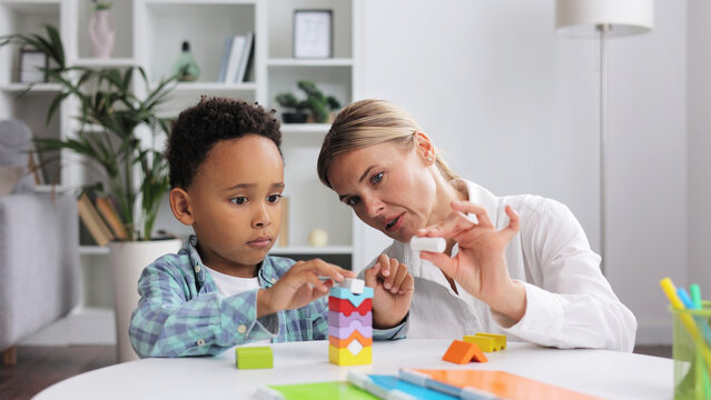 Assessment of mental development of children. Professional psychologist observes small multiracial boy playing with puzzle game, assessing his readiness for preschool. Exercises for kid with autism.