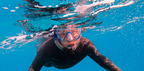 Man is diving, snorkeling with a mask and snorkel in the ocean.