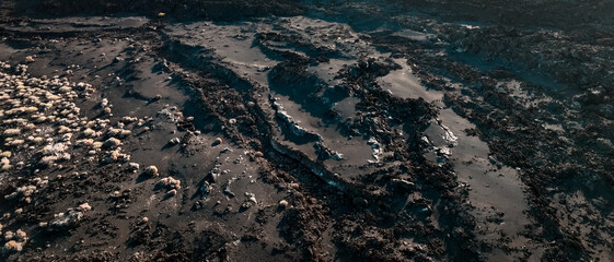 Black basalt lava formations, rocks, stones and sand, closeup view of volcanic dark terrain.