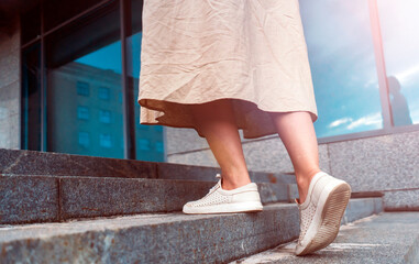 Young girl is walking up the stairs in the city, female legs in white shoes closeup.