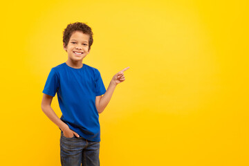 Cheerful black boy in blue shirt pointing at free space on yellow background © Prostock-studio