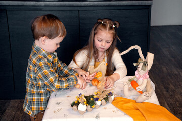 Children are preparing for Easter. Girl and Boy play Easter toys. Kids decorate the table, make handmade decorations for the Easter holiday. Eggs, a hare, Friends brother and sister positive emotions.