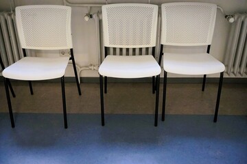 Innenausstattung von Warteraum mit drei weißen Stühlen vor Heizkörper in Krankenhaus