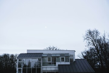 Modernes weiß-graues Haus mit Glasfassade und Flachdach vor weißem Himmel bei Frost und Kälte am...