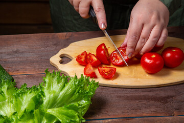 A woman's hand cuts a cherry tomato with a knife on a board on a table with vegetables