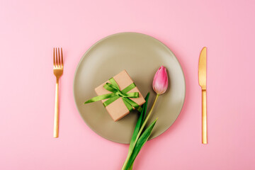 Gift box and pink tulip flower on light green plate on pink background Mothers day, womens day concept. Top view, flat lay