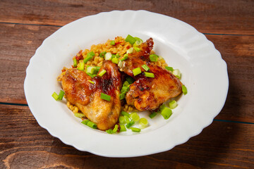 Chicken wings baked with bulgur, topped with green onions, garnished with cherry tomatoes on a white plate
