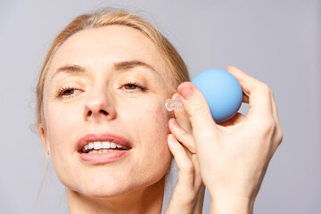 A young woman makes a face self-massage for the effect of lifting and rejuvenation while looking in...