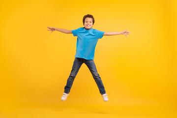 Fototapeta na wymiar Joyful boy jumping with arms outstretched, yellow backdrop