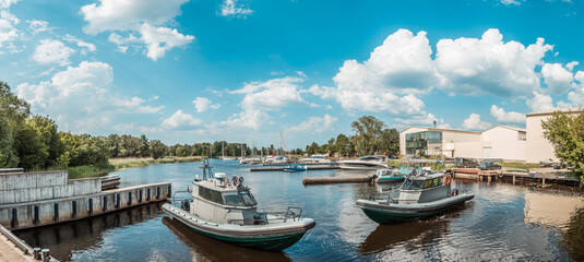 Panoramic view of military speed boats docked at a tranquil marina with sailing yachts under a blue sky with fluffy clouds