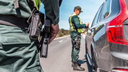 border patrol officer inspecting vehicle at checkpoint on sunny day with clear skies and long open...