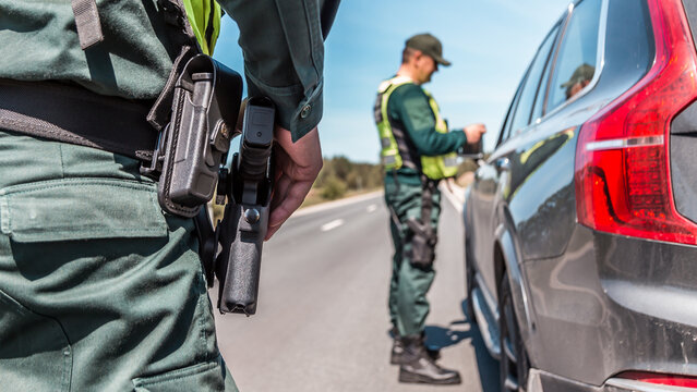 border patrol officer inspecting vehicle at checkpoint on sunny day with clear skies and long open road