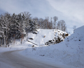 Snow covering rocky terrain and trees near a plowed road in winter in Muskoka Ontario