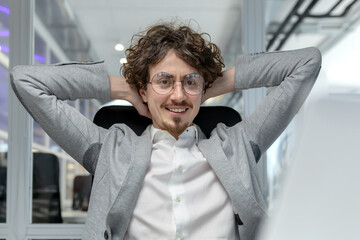 Smiling young adult businessman unwinding in an office chair displaying competence, satisfaction,...