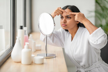 Portrait of upset beautiful young indian woman looking at mirror