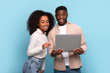 Black couple engaging with laptop together on blue background