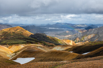 View at volcanic mountains with snow, green moss on hills and black lava on Icelandic highlands at...