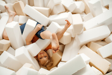 A young girl, playing and jumping in soft cubes in the dry pool of the game children's room for...