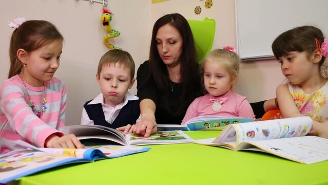 A teacher and children look at a textbook, teacher points in the book